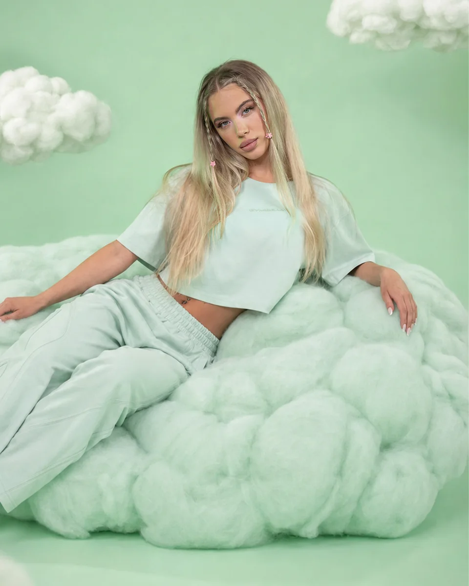 GymBeam-Model in einem mintfarbenen Outfit auf einer hellgrünen Wolke
